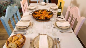 Mesa de comedor dispuesta con platos, vasos y un abundante plato de mariscos, rodeada de sillas.