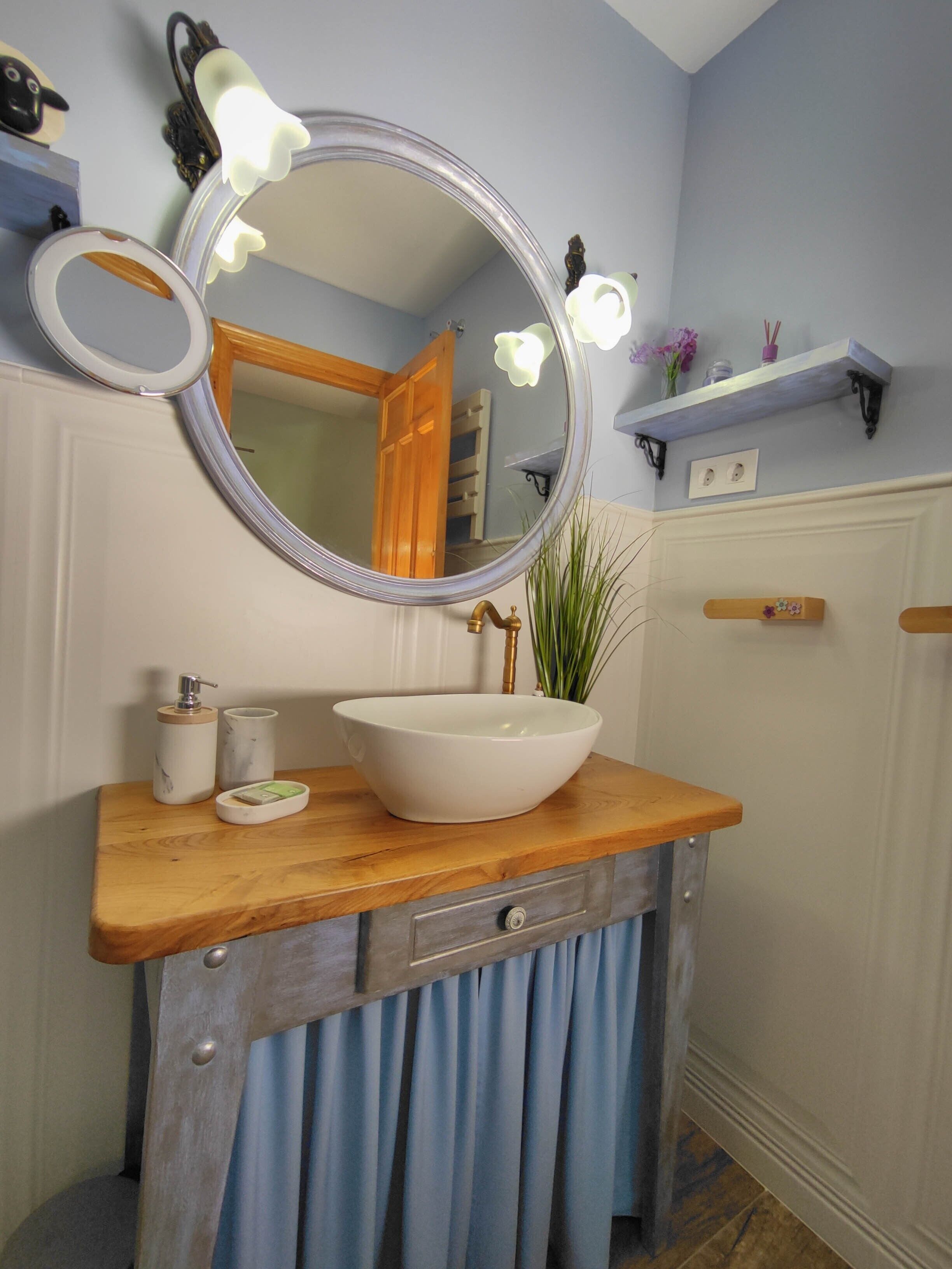 Une salle de bain avec un meuble-lavabo en bois, un grand miroir avec éclairage, un lavabo blanc et un rideau bleu.