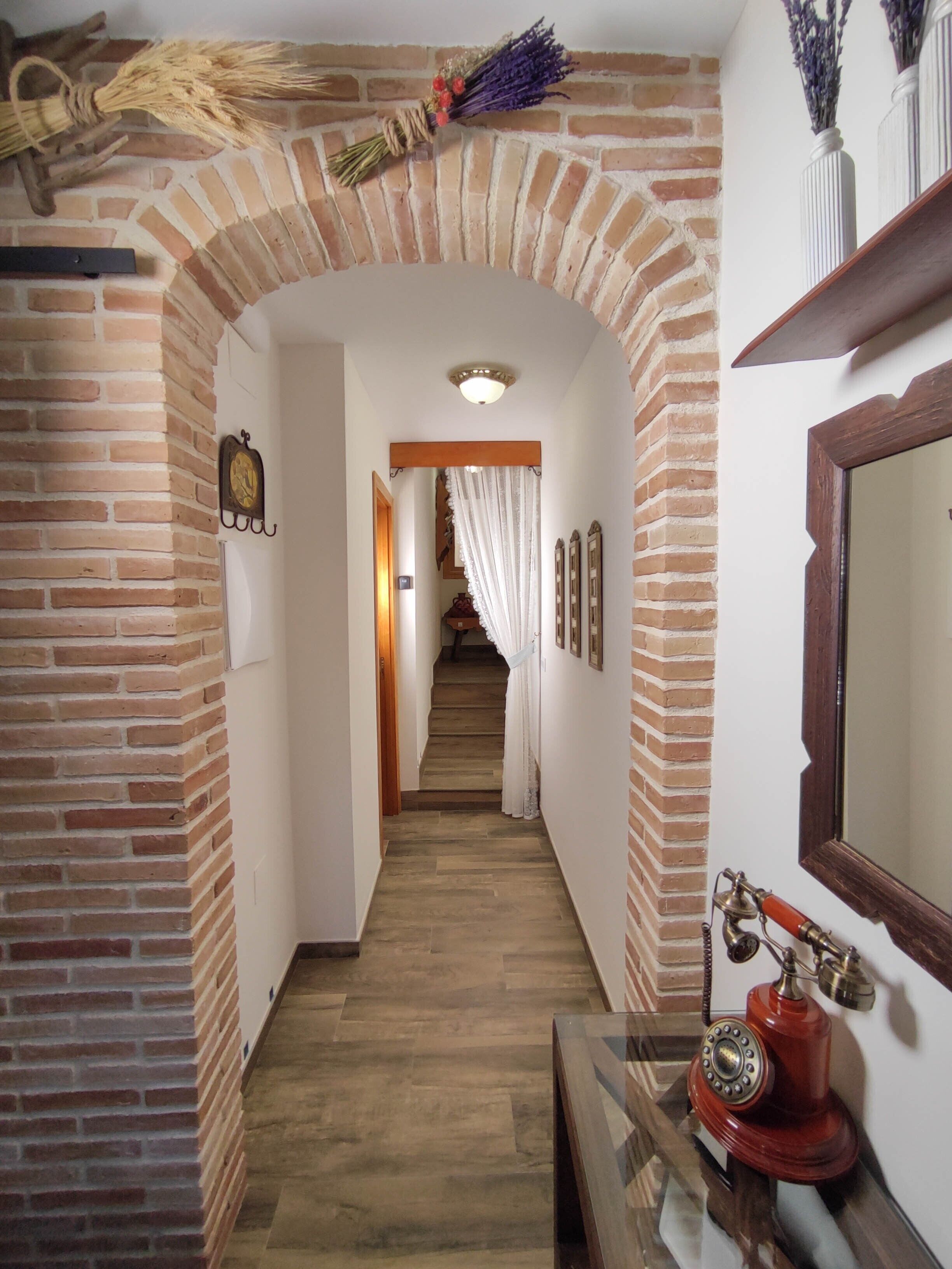 Un couloir aux murs en briques, avec un escalier en bois, un téléphone d’époque et un miroir accroché au mur.