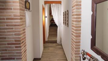 Un couloir aux murs en briques, avec un escalier en bois, un téléphone d’époque et un miroir accroché au mur.