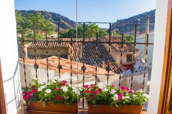 A balcony with terracotta tiles, potted flowers, and a view of terraced houses.