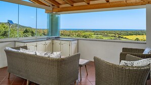 Un balcon doté de meubles en osier, d’une porte vitrée et offrant une vue sur un paysage verdoyant.