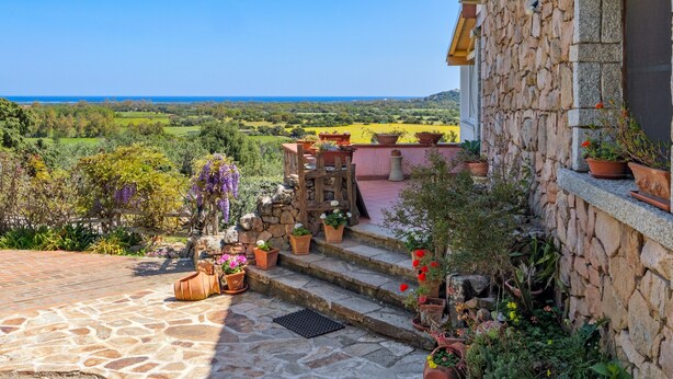 Un bâtiment en pierre doté d’un escalier en pierre menant à une terrasse agrémentée de plantes en pot et offrant une vue sur la campagne.