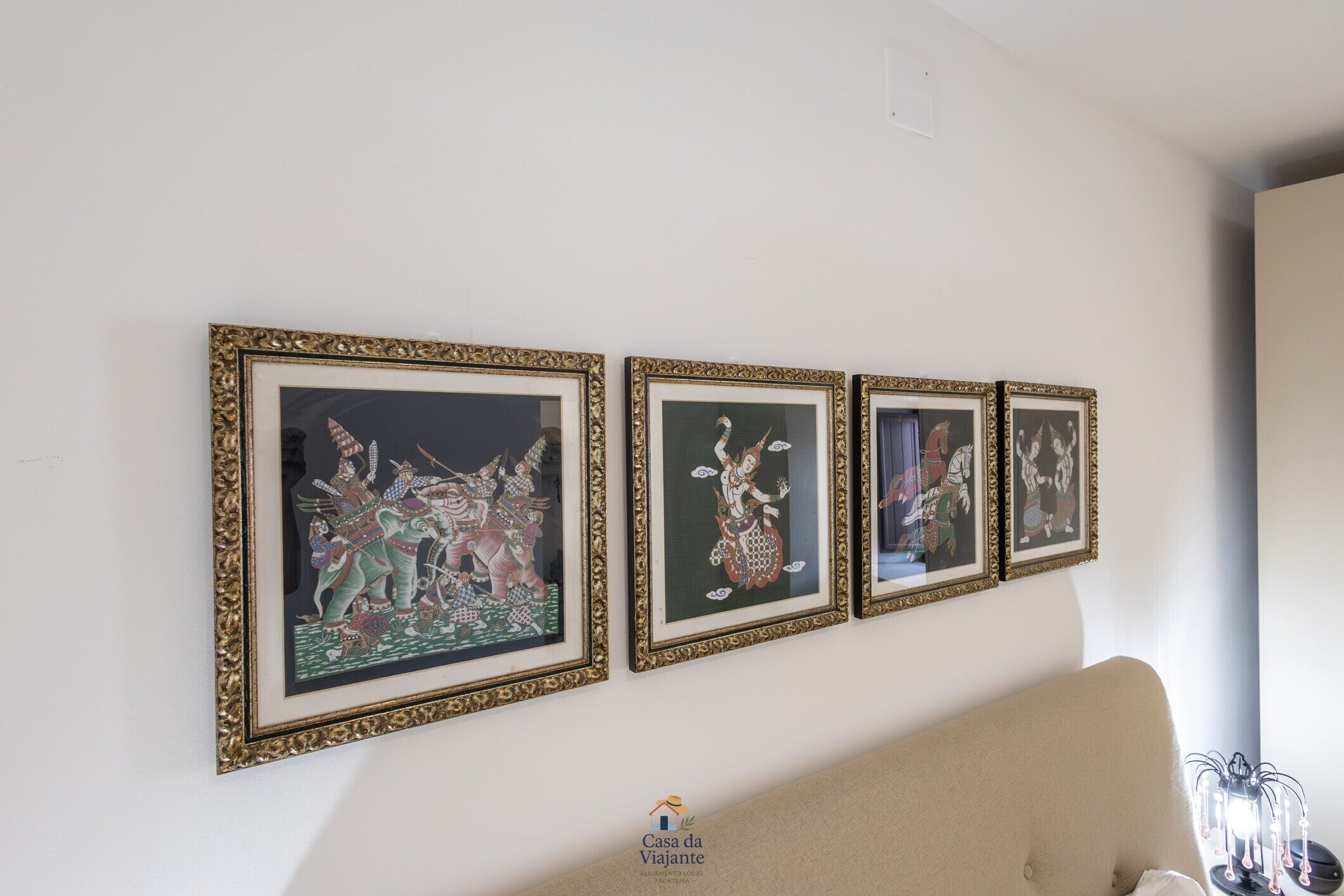 A wall with four framed artworks, a sofa, and a logo for 'Casa da Viajante.'