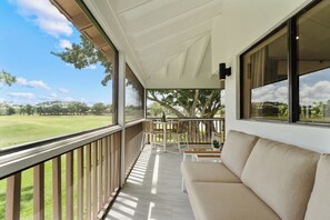 A balcony with a view of a golf course, a sofa, and a table with chairs. - Redesigned Lux Condo at PGA National | Golf & Pool (Palm Beach Gardens)