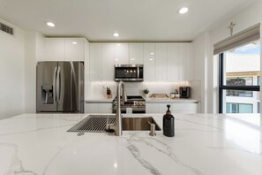 A modern kitchen with stainless steel appliances, white cabinetry, and a marble countertop. - Redesigned Lux Condo at PGA National | Golf & Pool (Palm Beach Gardens)