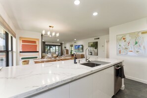 A modern kitchen with a marble countertop, a built-in sink, and a pendant light. - Redesigned Lux Condo at PGA National | Golf & Pool (Palm Beach Gardens)