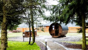 A rustic cabin with a barrel-shaped structure, surrounded by trees and a wooden fence.