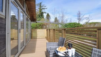 A deck with wicker furniture, a table with breakfast items, and a wooden fence.
