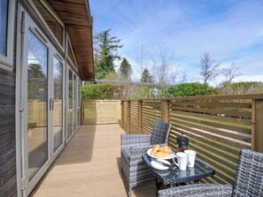 Eine Terrasse mit Korbmöbeln, einem Tisch mit Frühstücksgebäck und einem Holzzaun.