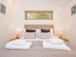 Una cama bien hecha con ropa de cama blanca y marrón, dos lámparas de noche y una ventana con persianas.