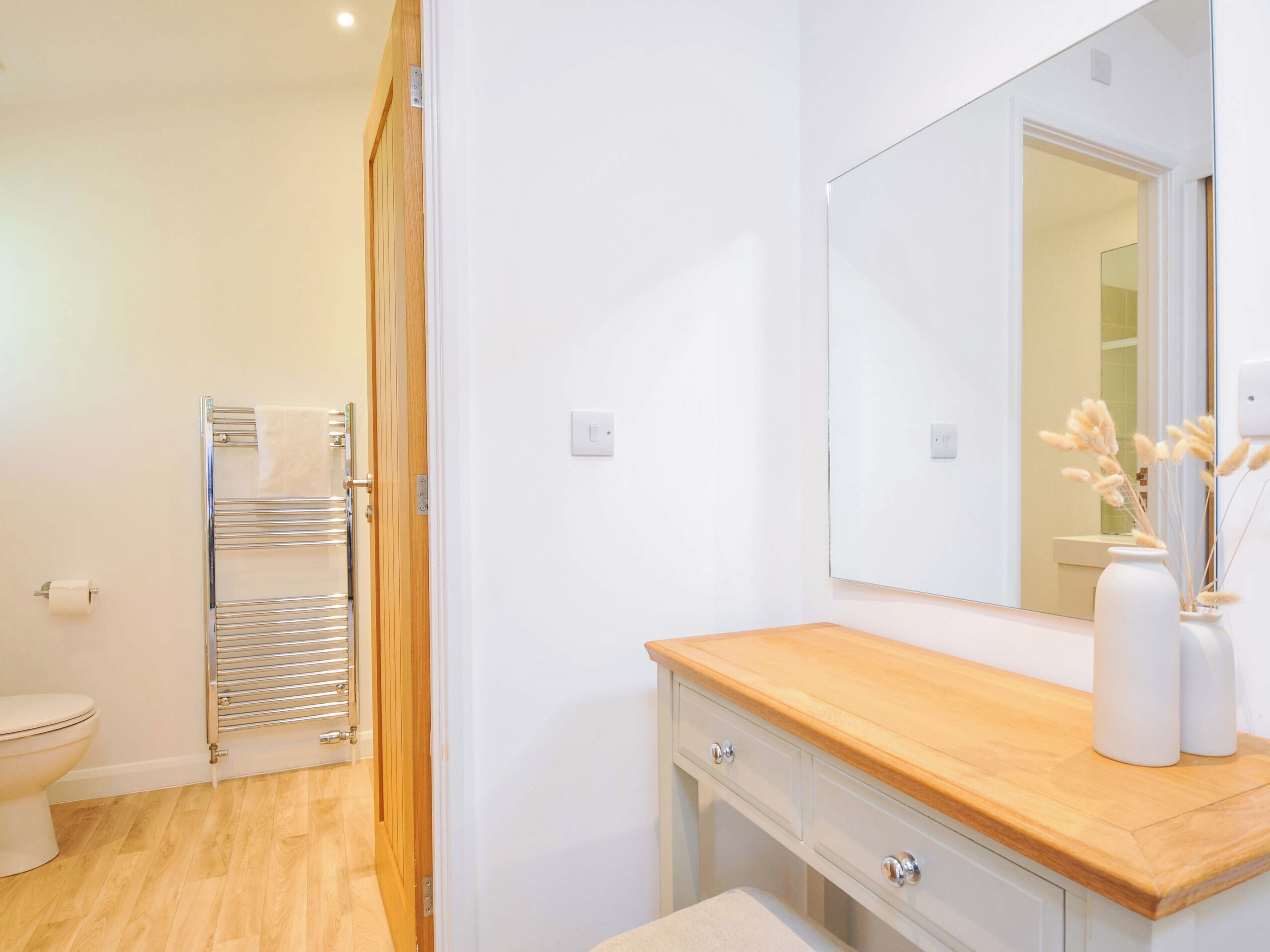 A bathroom with a wooden vanity, a mirror, a towel rack, and a toilet.
