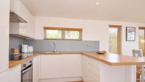 A modern kitchen with white cabinets, a wooden countertop, a built-in oven, and a window with blinds. - 3 Faraway Fields (Liskeard)