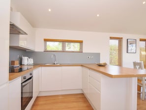 A modern kitchen with white cabinets, a wooden countertop, a built-in oven, and a window with blinds. - 3 Faraway Fields (Liskeard)