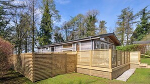 A single-story wooden cabin with a sloped roof, a fenced yard, and a clear view of the surrounding trees. - 3 Faraway Fields (Liskeard)