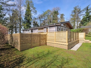 A single-story wooden cabin with a sloped roof, a fenced yard, and a clear view of the surrounding trees. - 3 Faraway Fields (Liskeard)