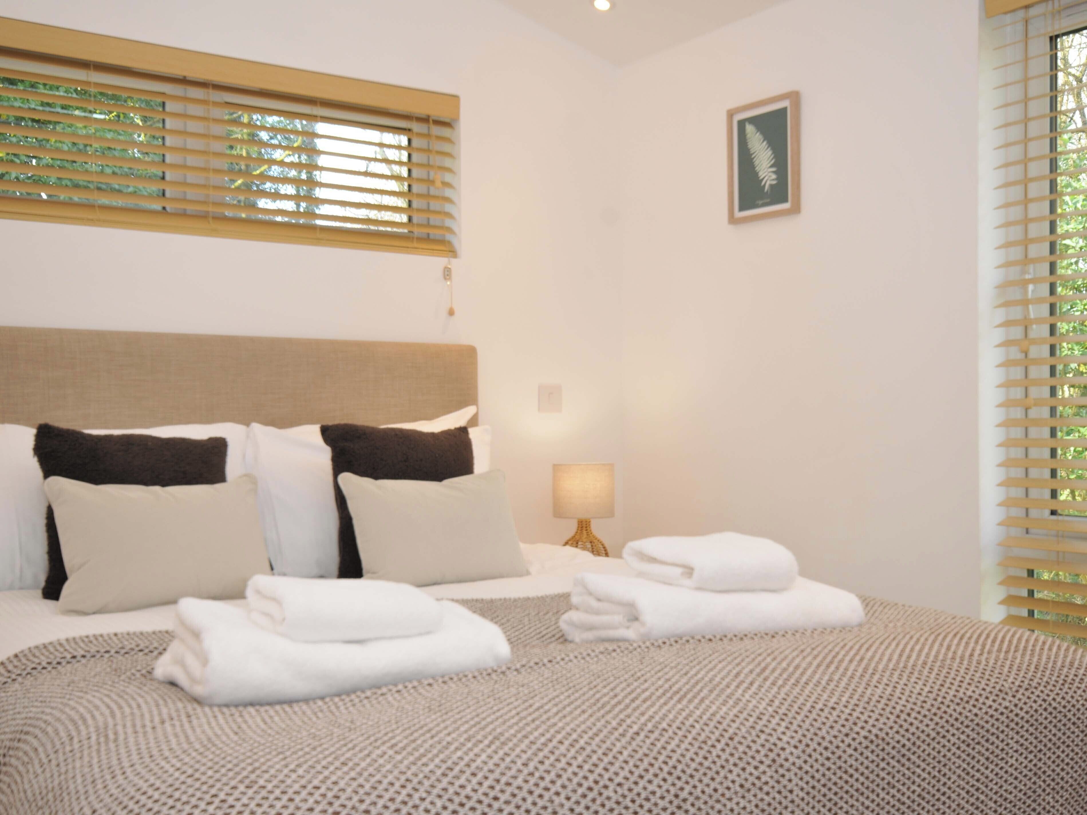 Una cama bien hecha con ropa de cama blanca y marrón, una lámpara de noche y una impresión botánica enmarcada en la pared.