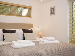Un lit bien fait, avec une literie blanche et marron, une lampe de chevet et une estampe botanique encadrée accrochée au mur.