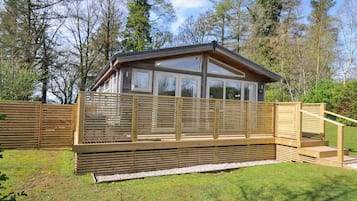 Una cabaña de madera con terraza, rodeada de árboles.