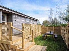 Una terraza de madera con una mesa de picnic y una escalera que lleva a un edificio.