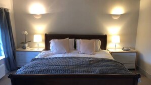 Una cama con cabecera de madera, dos mesitas de noche con lámparas, y una planta en maceta sobre una de ellas.