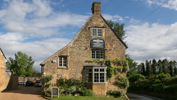 Un edificio de piedra con un letrero que dice 'The Ebrington Arms' y un letrero más pequeño que dice 'Our Duck Table'.