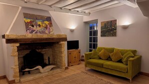 Una sala de estar acogedora con chimenea de piedra, un sofá verde y obras de arte en las paredes.