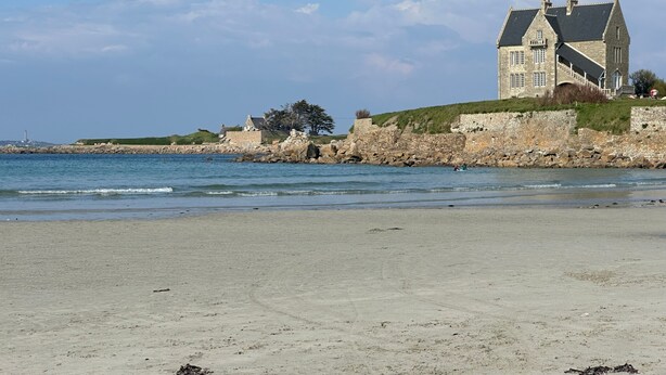 Un edificio frente al mar con fachada de piedra, un balcón grande y vistas al océano.