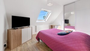 Un dormitorio con televisión, ventana, cama y espejo.