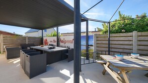 Un patio exterior con mobiliario de mimbre, una mesa de madera y vista al mar.