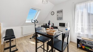 Una habitación moderna y bien iluminada con mesa de comedor, sillas, una cinta de correr y una cocina equipada con electrodomésticos.
