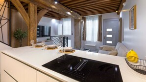 Una cucina moderna con piano cottura a induzione nero, travi in legno e zona pranzo con divano e una ciotola di frutta gialla.