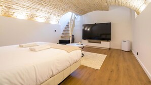Una camera da letto con un letto, una TV, un muro bianco, un pavimento in legno e un soffitto con motivo decorativo.