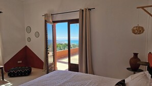 A bedroom with a large bed, a view of the sea, and a balcony.