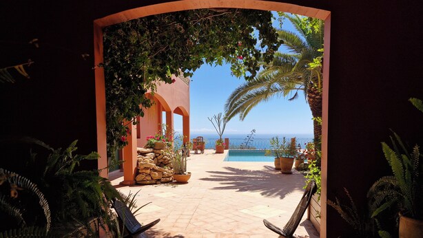 An outdoor patio with a pool, potted plants, and a view of the sea.