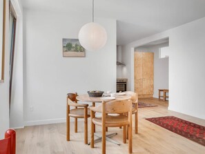A modern dining area with a round table, wooden chairs, a hanging light fixture, and a kitchen in the background. - 4 Star Holiday Home in Lokken (Lokken)