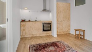 A compact kitchen with a built-in oven, wooden cabinets, and a small wooden stool. - 4 Star Holiday Home in Lokken (Lokken)