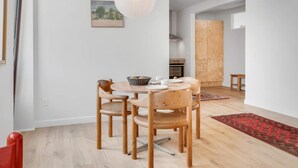 A dining area with a round table, four wooden chairs, a hanging light fixture, a kitchen in the background, and a red patterned rug on the floor. - 4 Star Holiday Home in Lokken (Lokken)