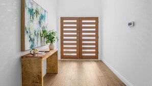 Ein Flur mit Holzboden, einem hölzernen Konsolentisch mit Pflanze, einem großen abstrakten Gemälde und einem Paar Holztüren.