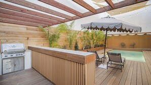 Eine Außenpatio mit Holzdeck, Grill, Schwimmbecken und Liegestühlen.