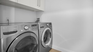Ein Waschraum mit zwei Waschmaschinen mit Frontlader, einem weißen Schrank darüber und einer Steckdose an der Wand.