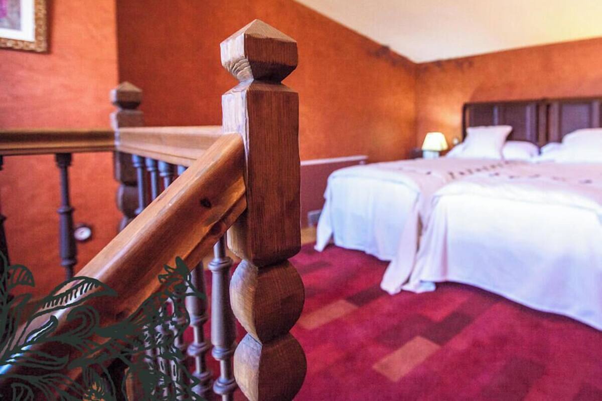 A hotel room with a wooden staircase railing, a bed with white bedding, and a red carpeted floor.