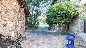 Un chemin de pierres mène à un bâtiment rustique, orné d’une lanterne suspendue et d’une lanterne bleue sur la droite.