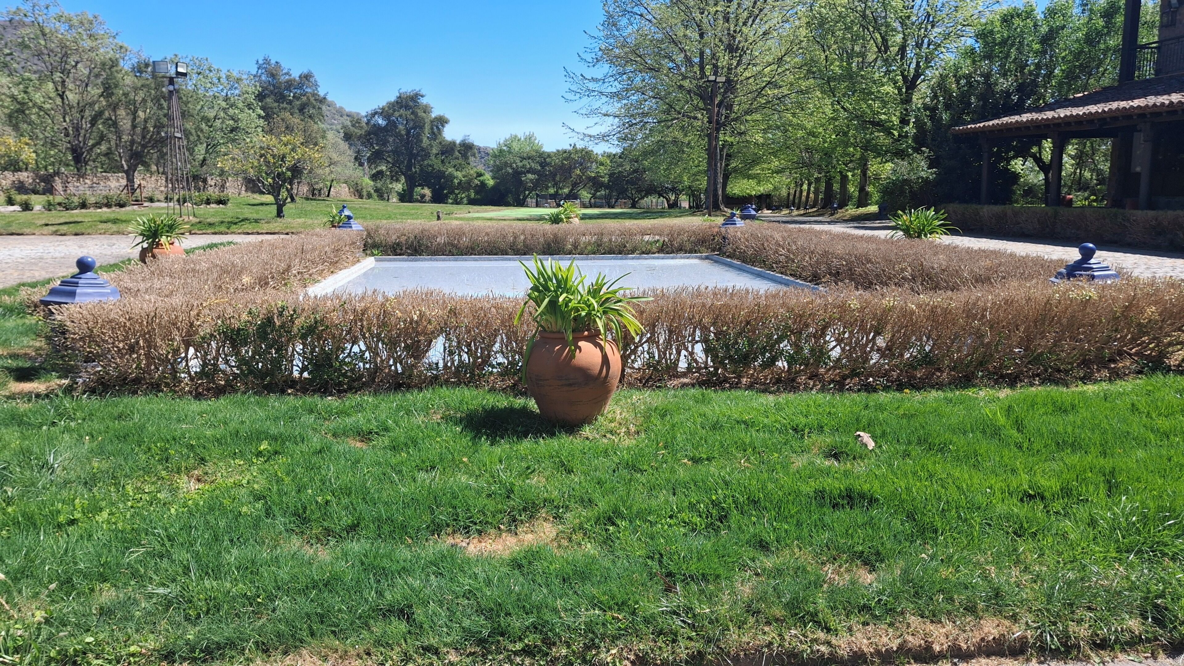 Un jardín ajardinado con una fuente central, rodeado de setos cuidados y césped ordenado.