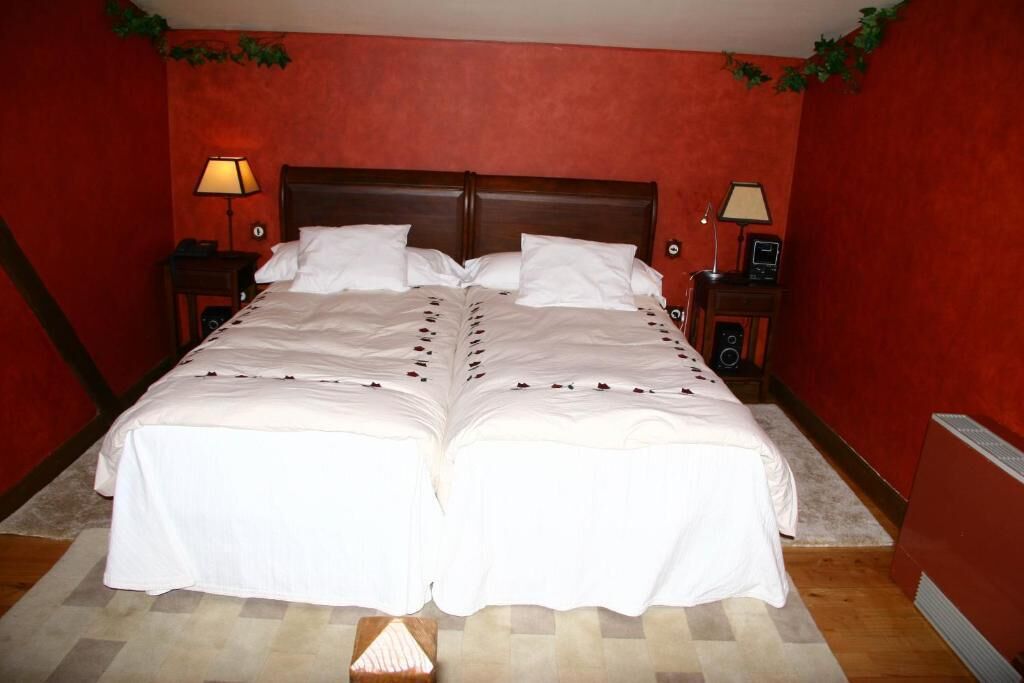 Una cama doble con sábanas blancas, dos mesitas de noche con lámparas y una pared roja.