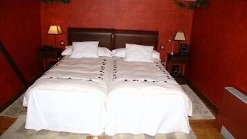 Una cama doble con sábanas blancas, dos mesitas de noche con lámparas y una pared roja.