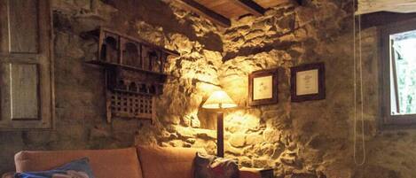 Ein Zimmer mit Steinwänden und Holzbalkendecke, mit einer Couch, einer Lampe und gerahmten Bildern an der Wand.