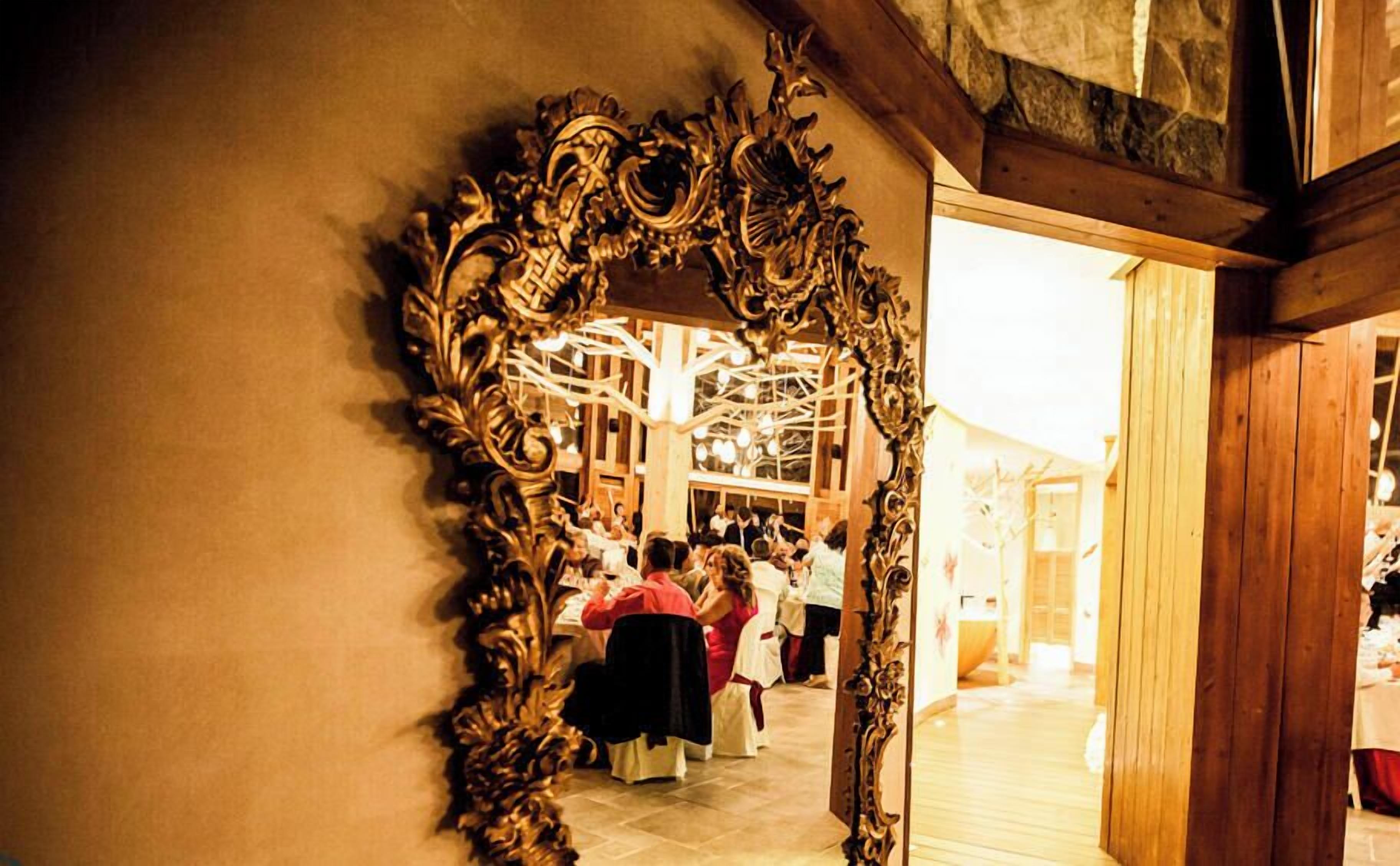 A room with a large ornate mirror, wooden beams, and a group of people seated at a table.