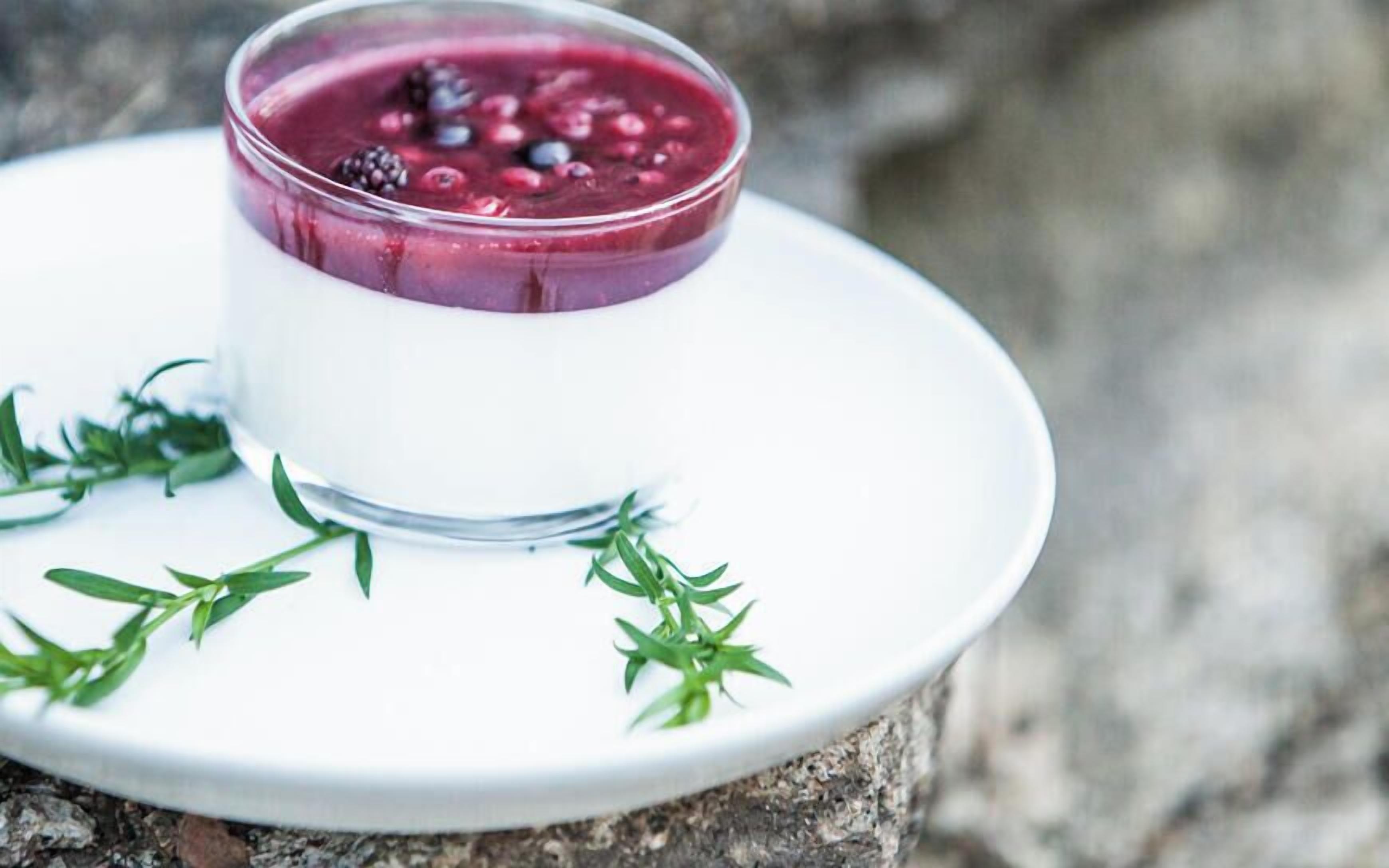 Un postre en un bol de vidrio sobre un plato blanco, con guarnición verde, sobre una superficie de piedra.