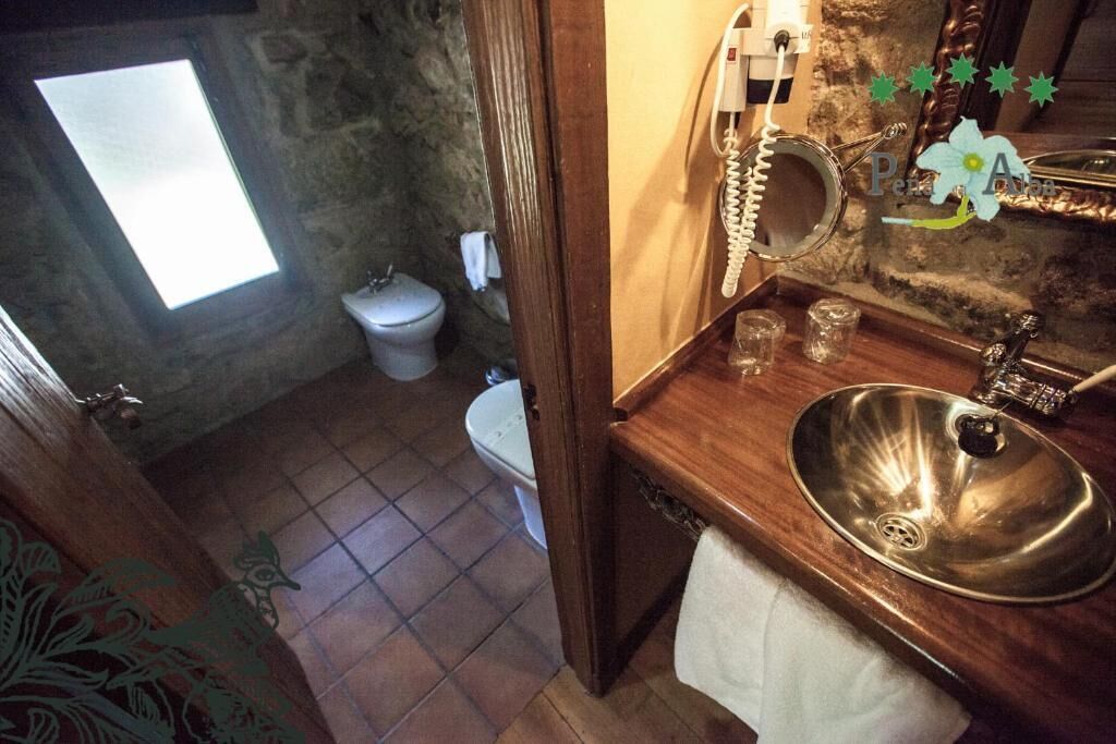 Een badkamer met een stenen muur, een houten wastafelmeubel, een wastafel, een toilet en een raam.